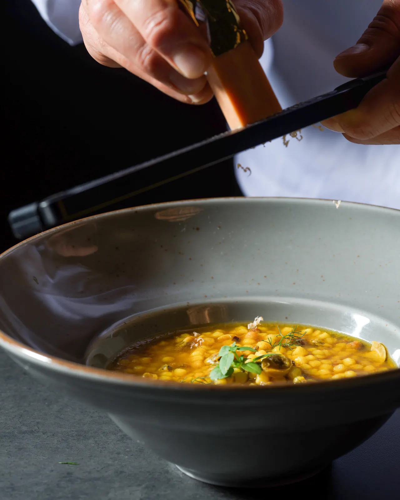Mani che tengono il Lingotto e lo grattugiano su una pasta in brodo