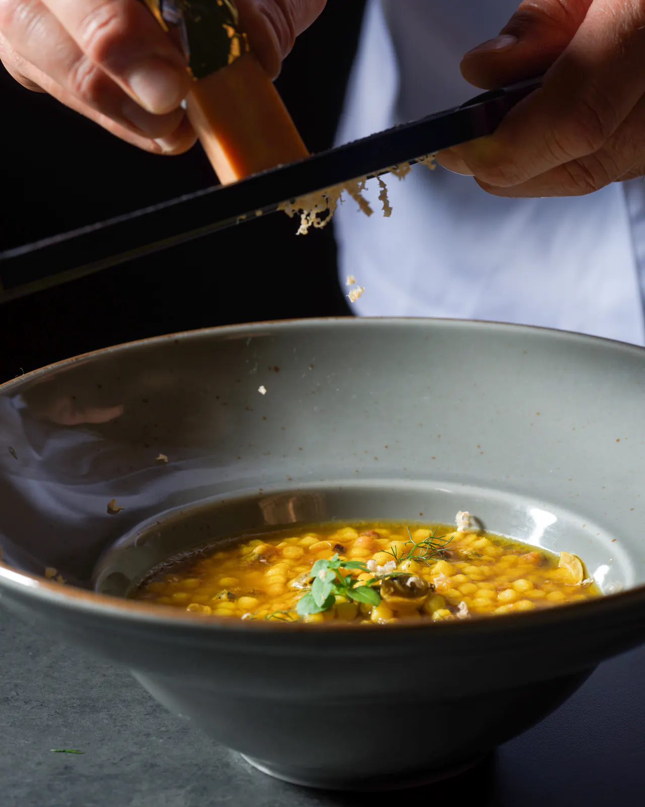 Mani in giacca da cuoco grattugiano il Lingotto su una pasta in brodo, in una fondina grigia